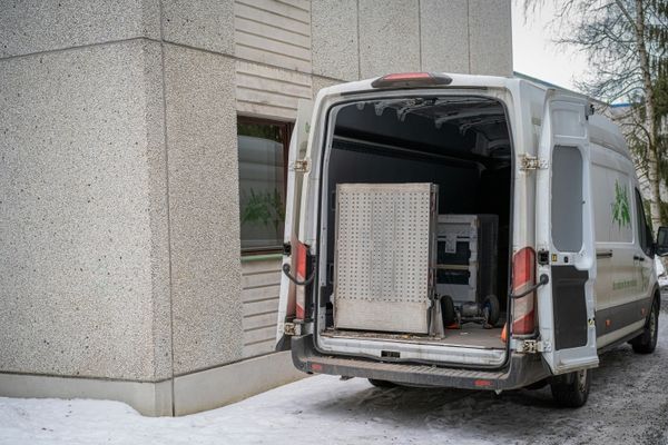 Weißer Lieferwagen mit geöffneter Heckklappe, der vor einem Betongebäude auf schneebedecktem Boden geparkt ist.