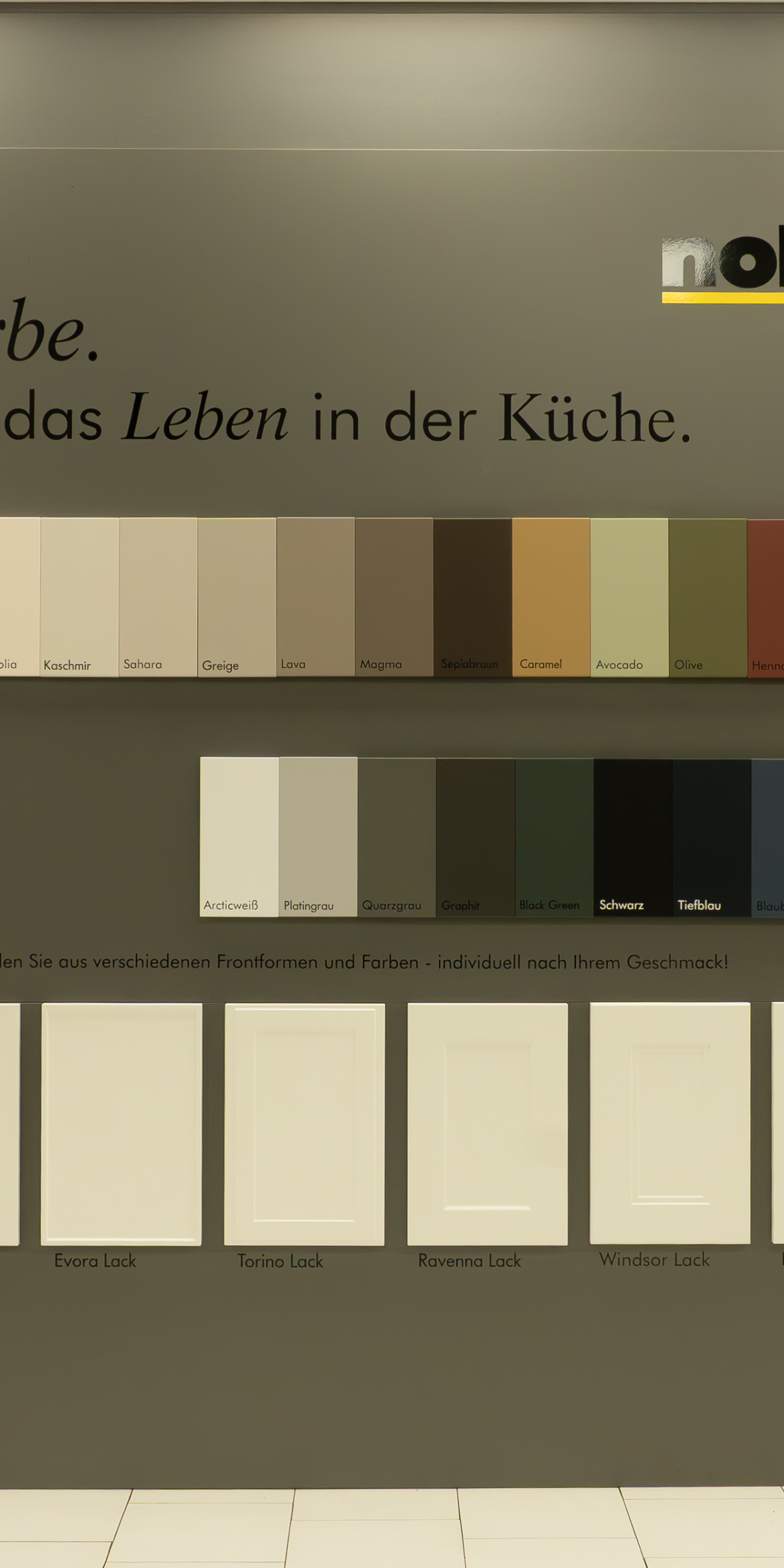 Farbmuster und Küchenfronten-Auswahl mit Namen wie Kaschmir, Sahara, Lava und Windsor Lack in einer Ausstellung.