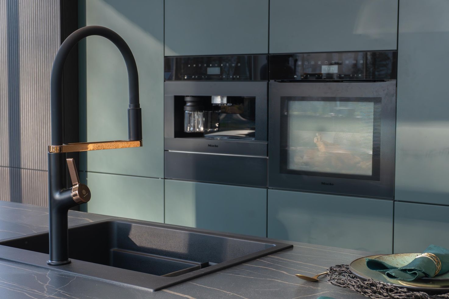 Moderne Küchenarmatur mit schwarzem und goldenem Design neben Spüle, eingebauter Kaffee- und Backofen in grauer Küche.