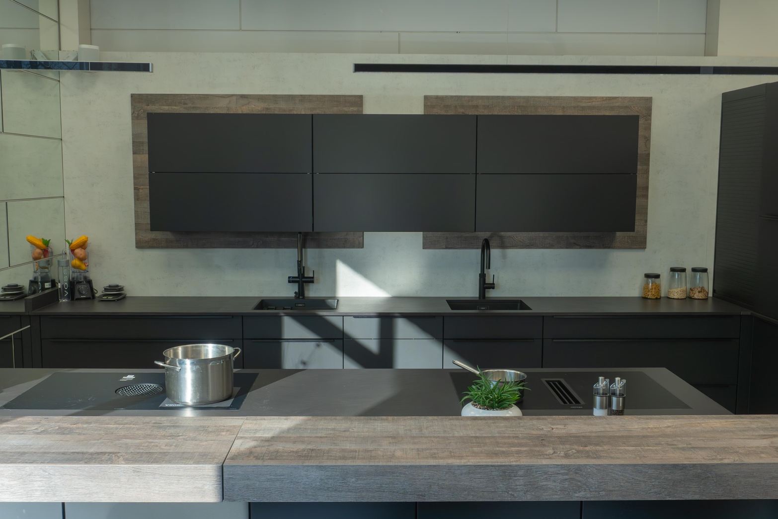 Moderne Küche mit schwarzen Schränken, zwei Spülbecken, Kochfeld mit Topf und einem Küchenblock aus Holz.