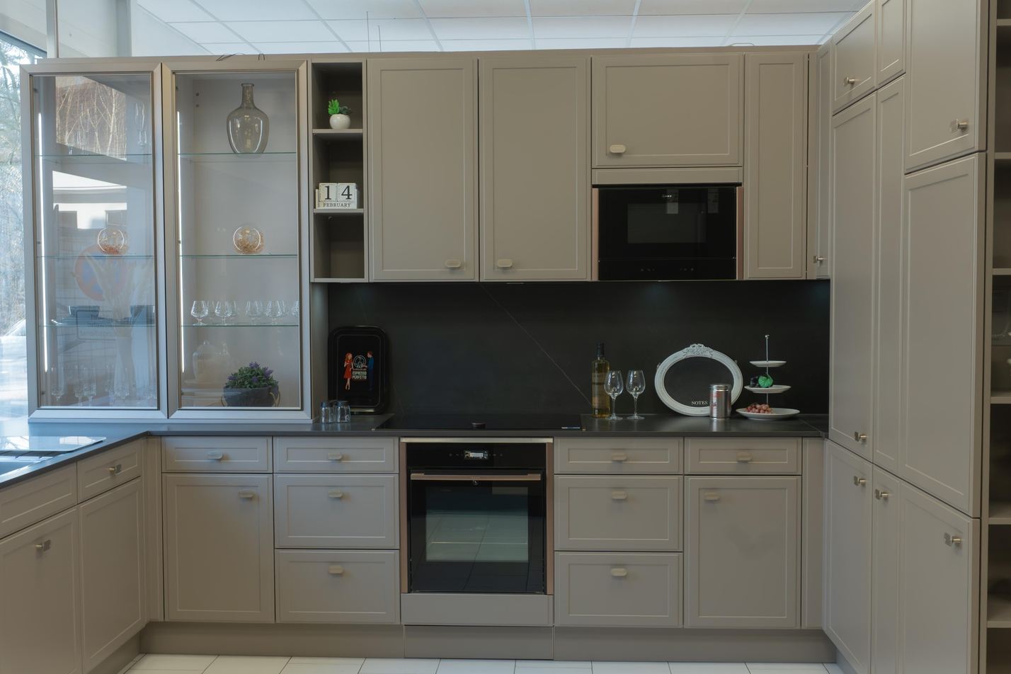 Moderne graue Einbauküche mit Glasvitrine, eingebautem Backofen, Mikrowelle und Dekoration auf der Arbeitsplatte.