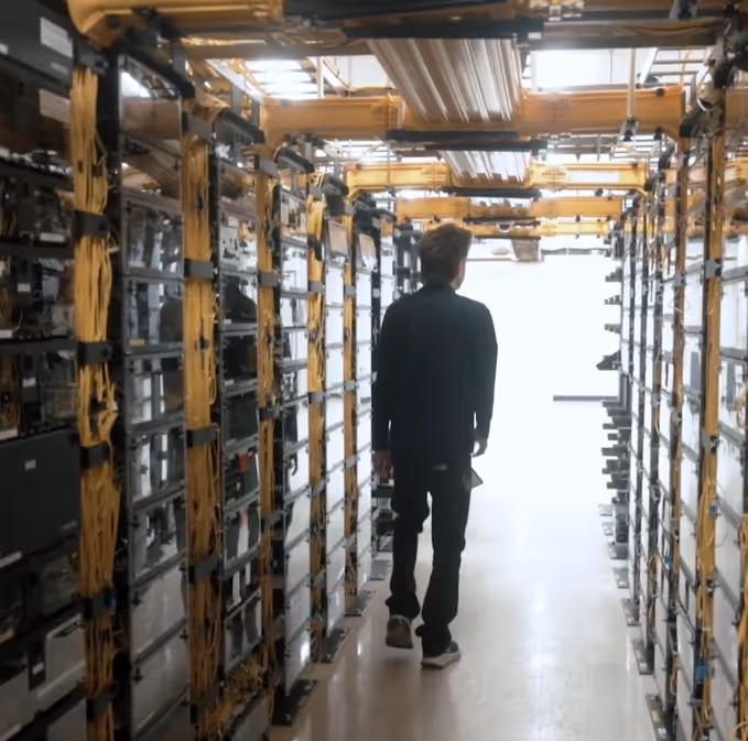 Person walking down aisle between rows of server racks with yellow cables in a data center.