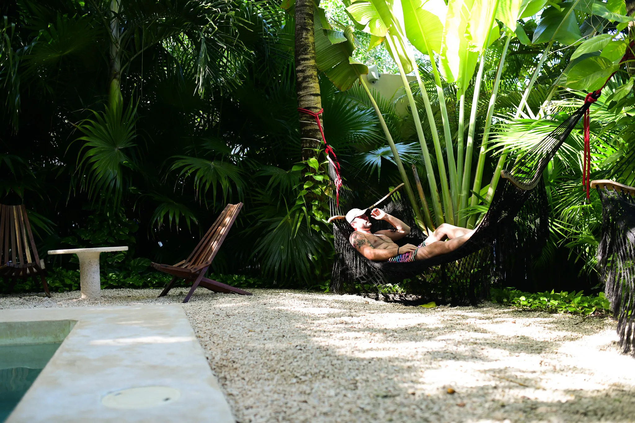 Guest relaxing in a poolside hammock among tropical plants during a resort lifestyle shoot.