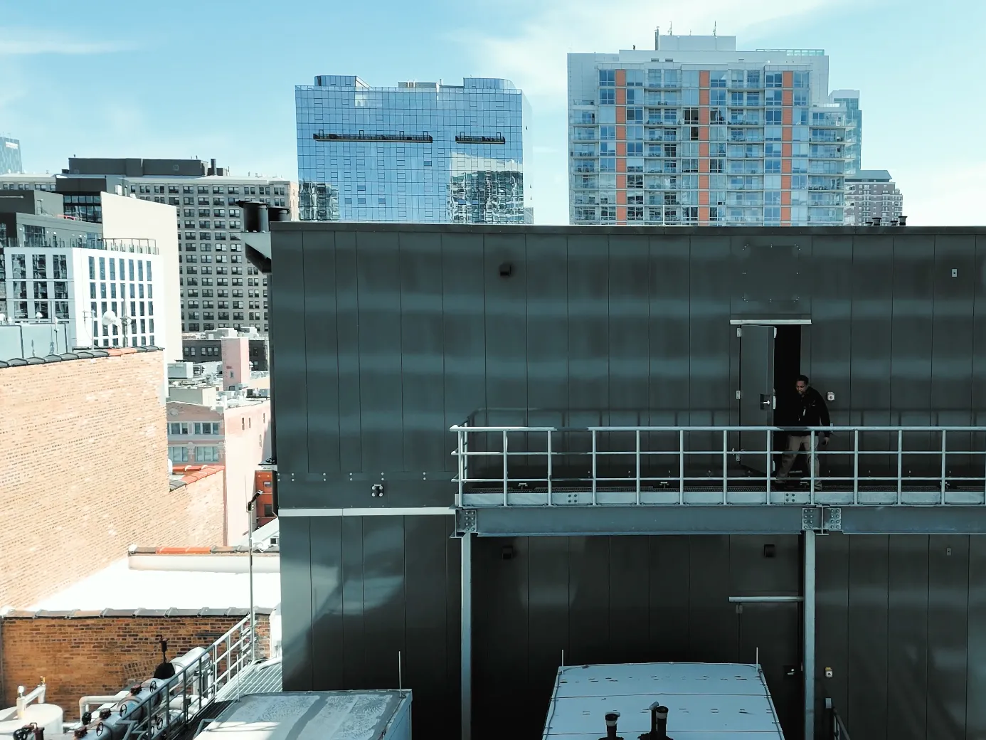 Person exiting gray rooftop building with city skyline in background under clear blue sky.