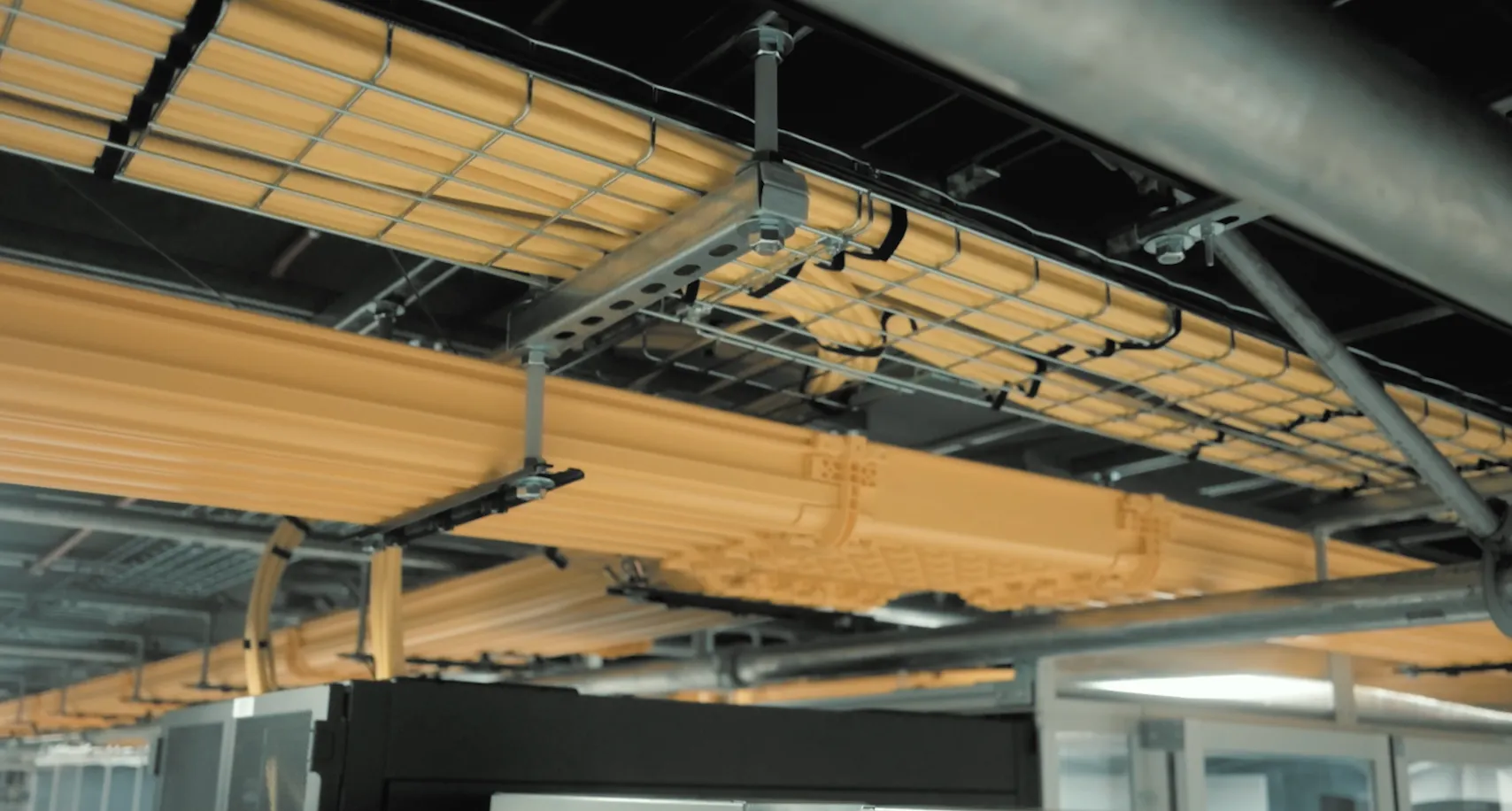 Close-up of yellow fiber optic cables organized and mounted on a ceiling cable tray in a server room.