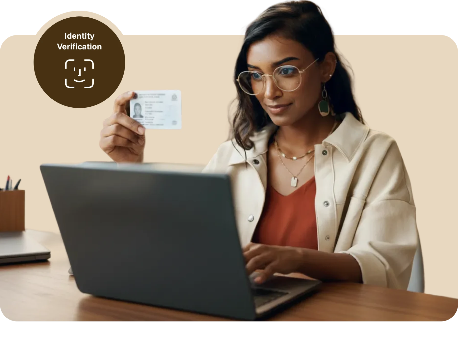 Woman holding ID card up to laptop for identity verification on beige background.
