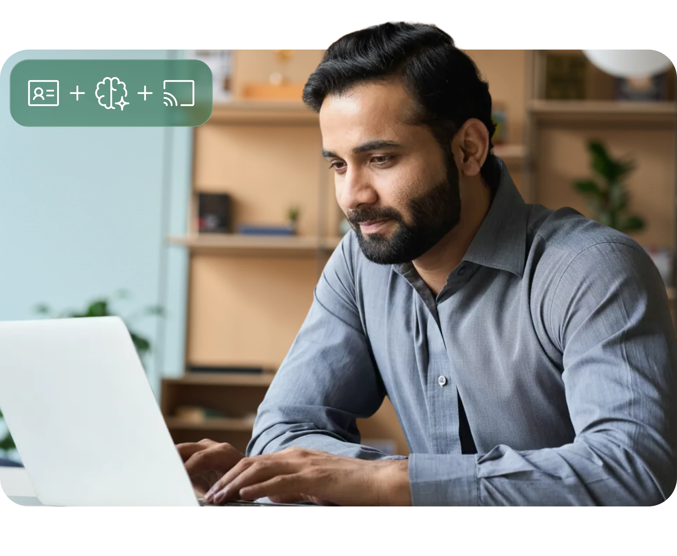 Bearded man in a gray shirt working on a white laptop in a modern office setting.