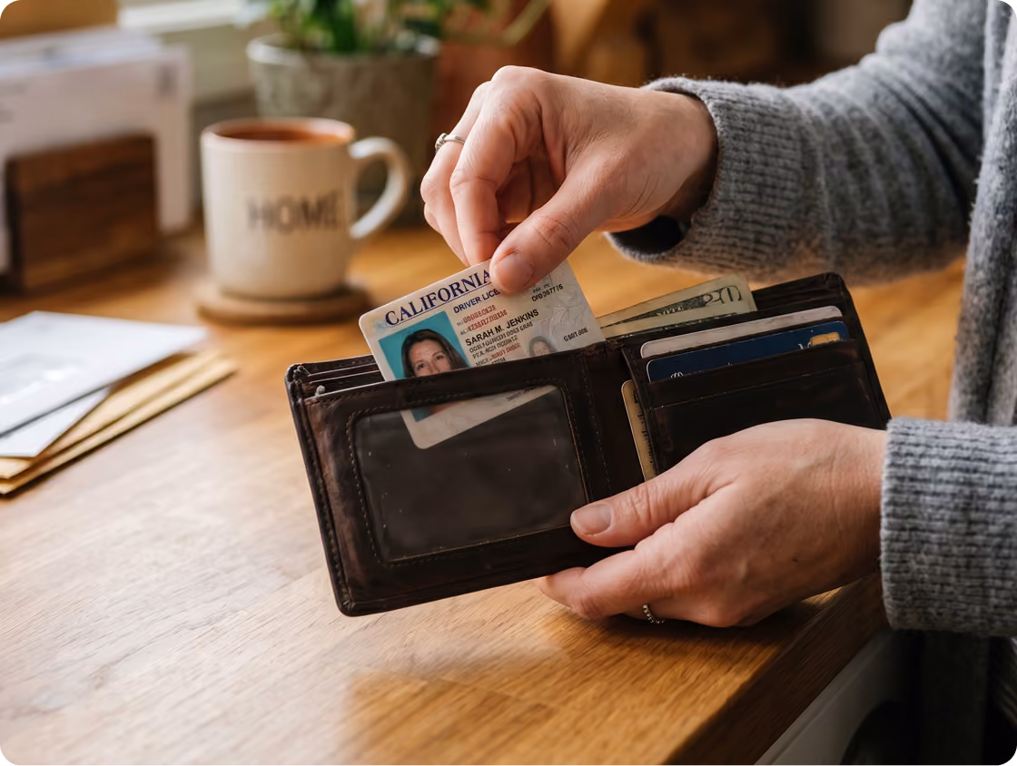 Person holding a wallet and pulling out a California driver's license, with a coffee mug in the background.