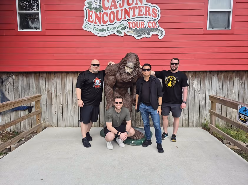 Four men posing with a Bigfoot statue outside Cajun Encounters Tour Co. building.