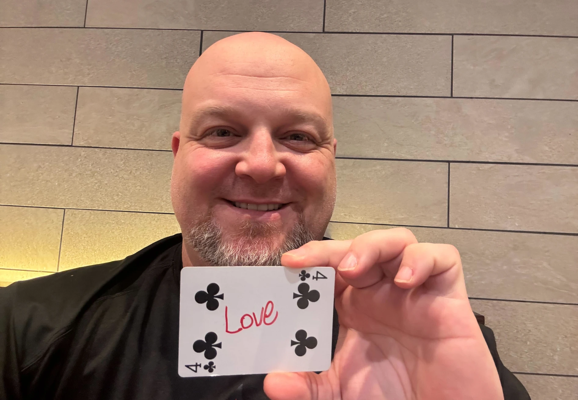 Smiling man holding a 4 of clubs card with the word Love written in red.