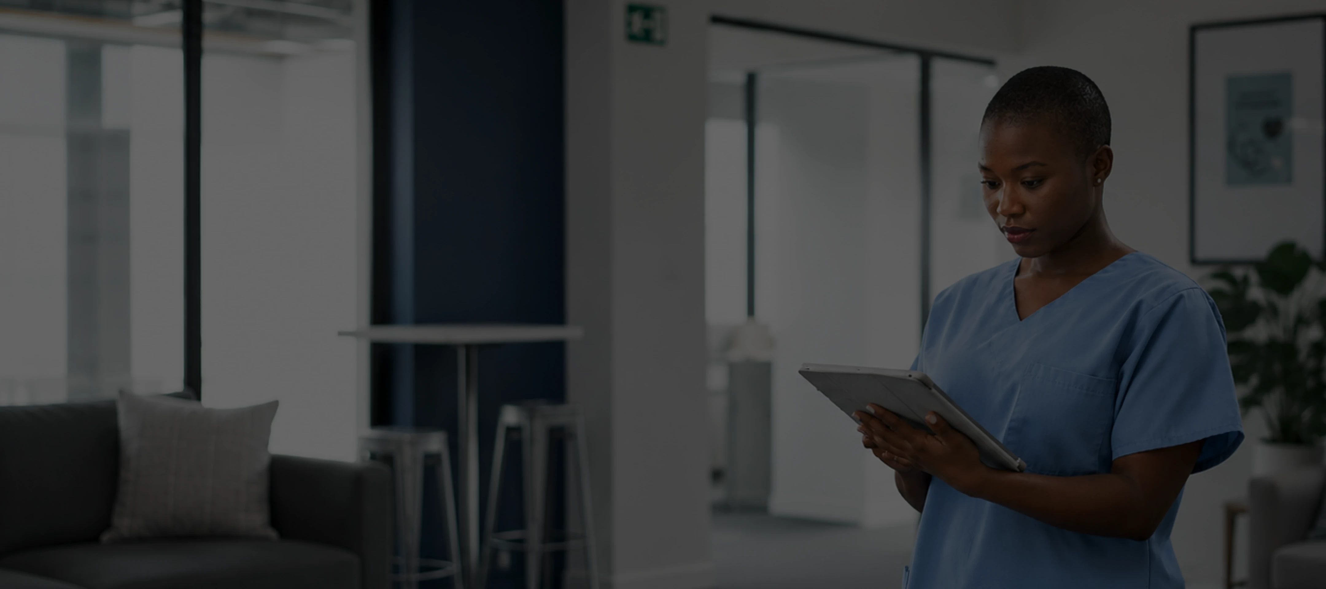 Healthcare worker in blue scrubs holding and reading a tablet device indoors.