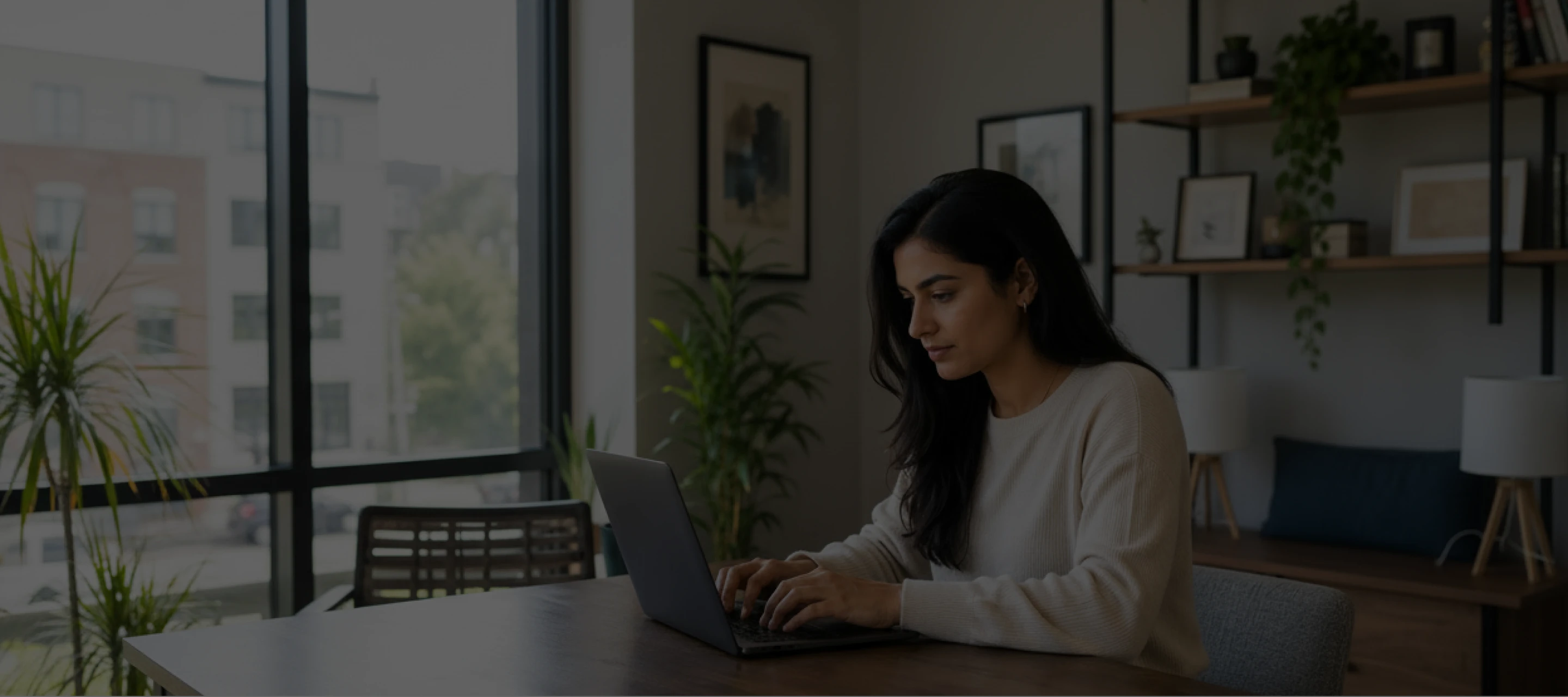 Woman with long dark hair working on a laptop at a wooden desk in a modern home office.