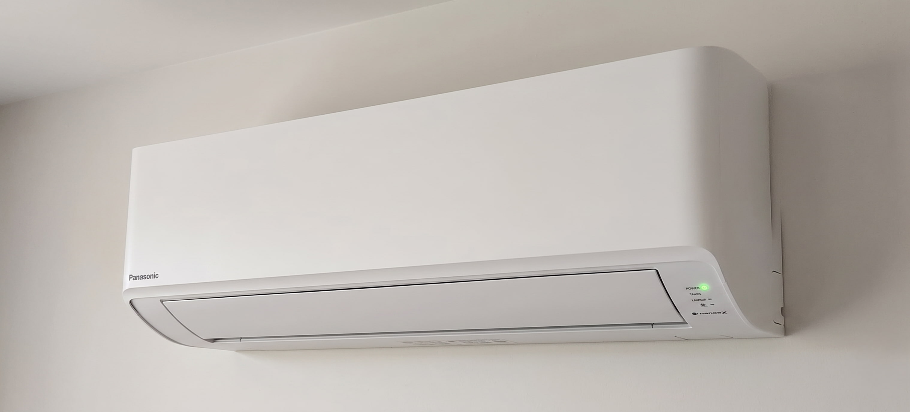 Panasonic Nanoe-X wall-mounted heat pump indoor unit with green power light illuminated on the indicator panel