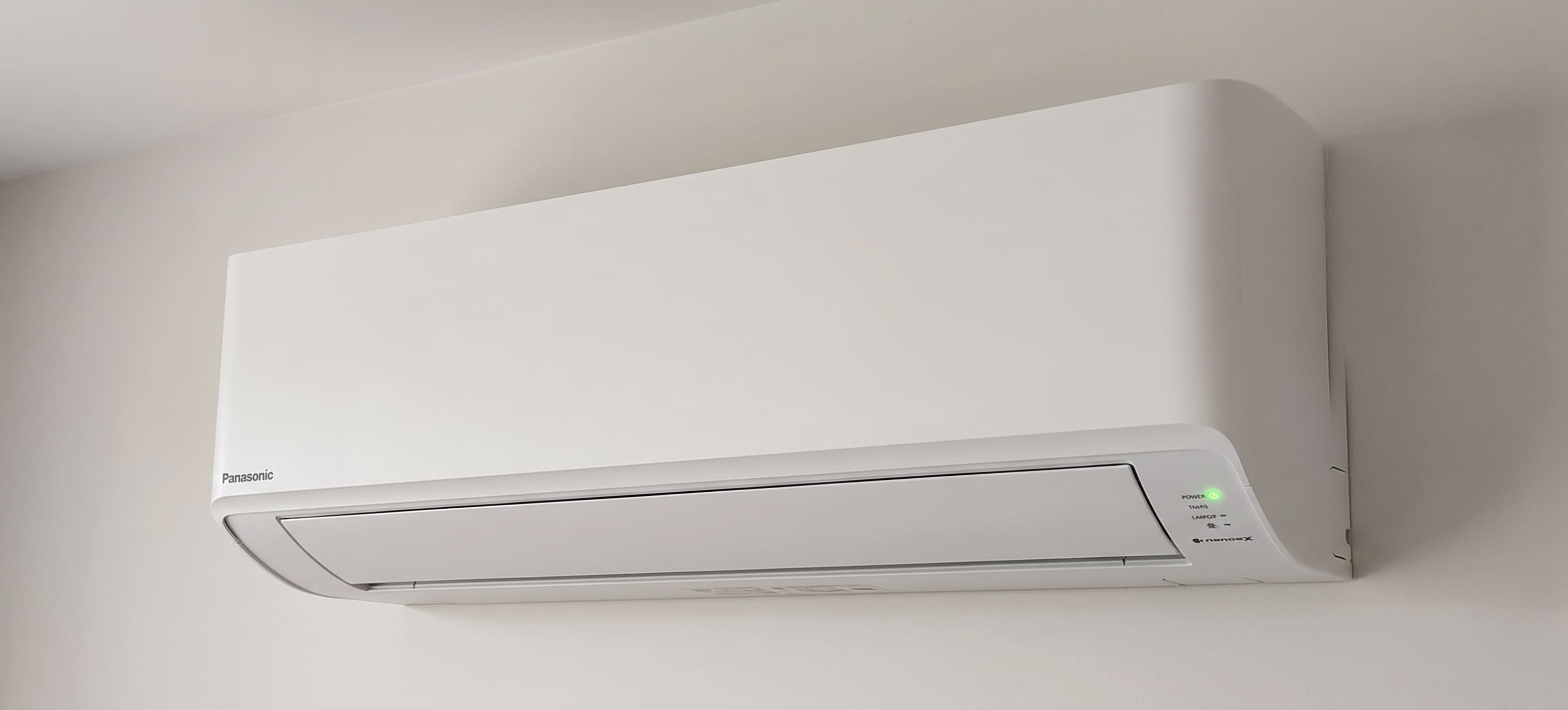 Panasonic Nanoe-X wall-mounted heat pump indoor unit with green power light illuminated on the indicator panel