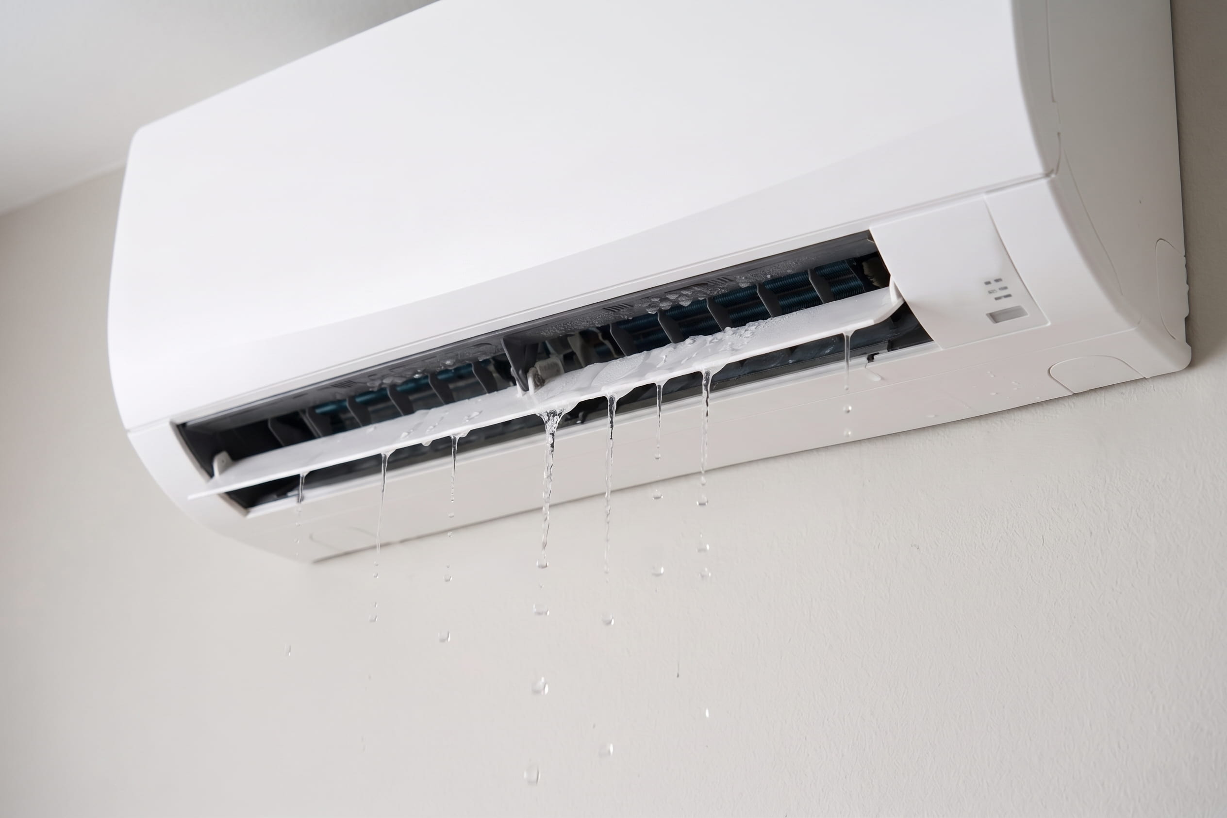 Wall-mounted heat pump leaking water from the indoor unit, with multiple streams of water dripping from the front casing onto the wall below