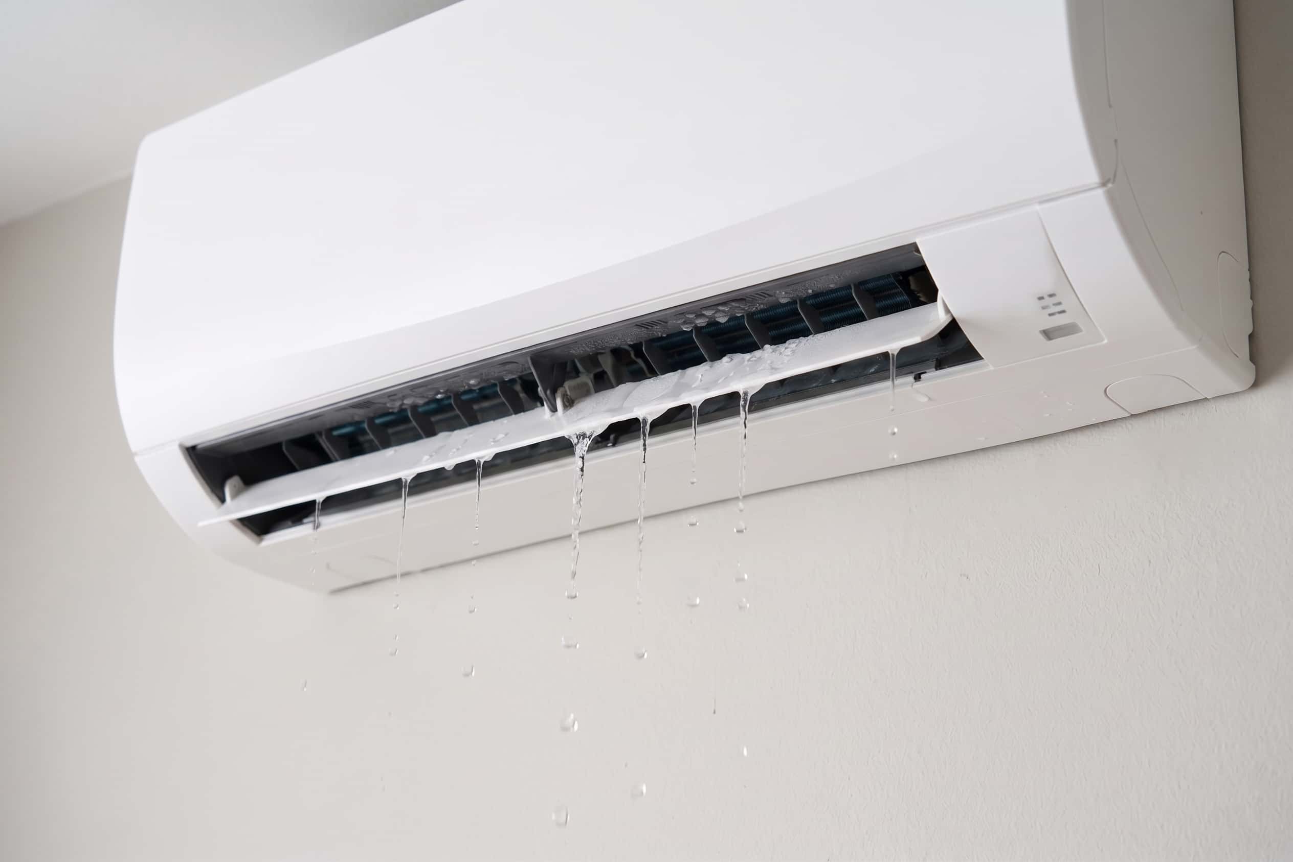Wall-mounted heat pump leaking water from the indoor unit, with multiple streams of water dripping from the front casing onto the wall below