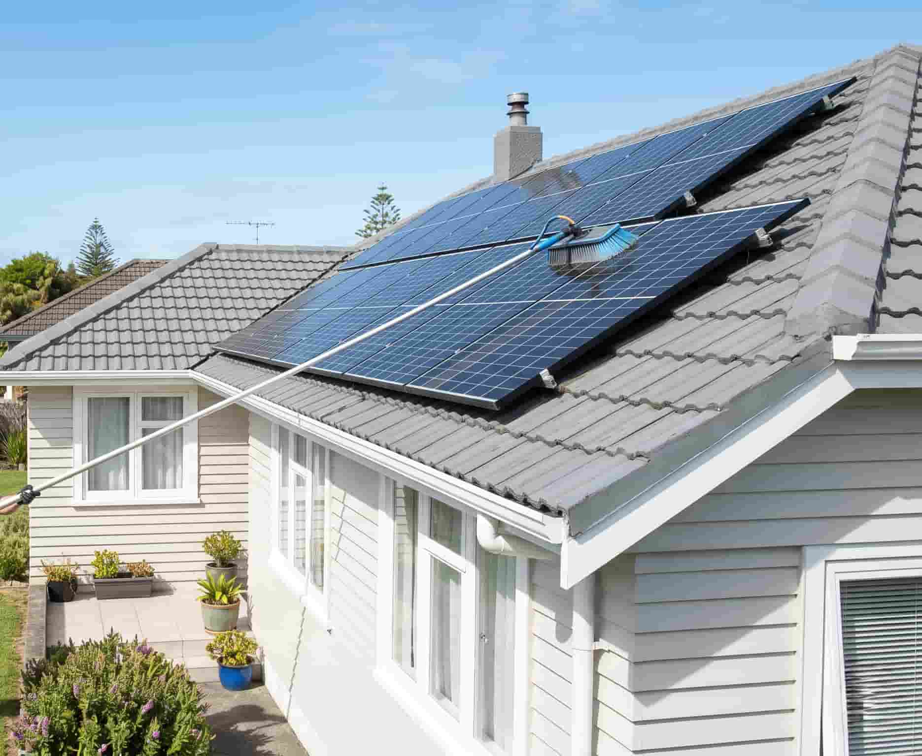 Solar panels being cleaned with a soft-bristle brush on an extension pole on a residential roof in Auckland, New Zealand