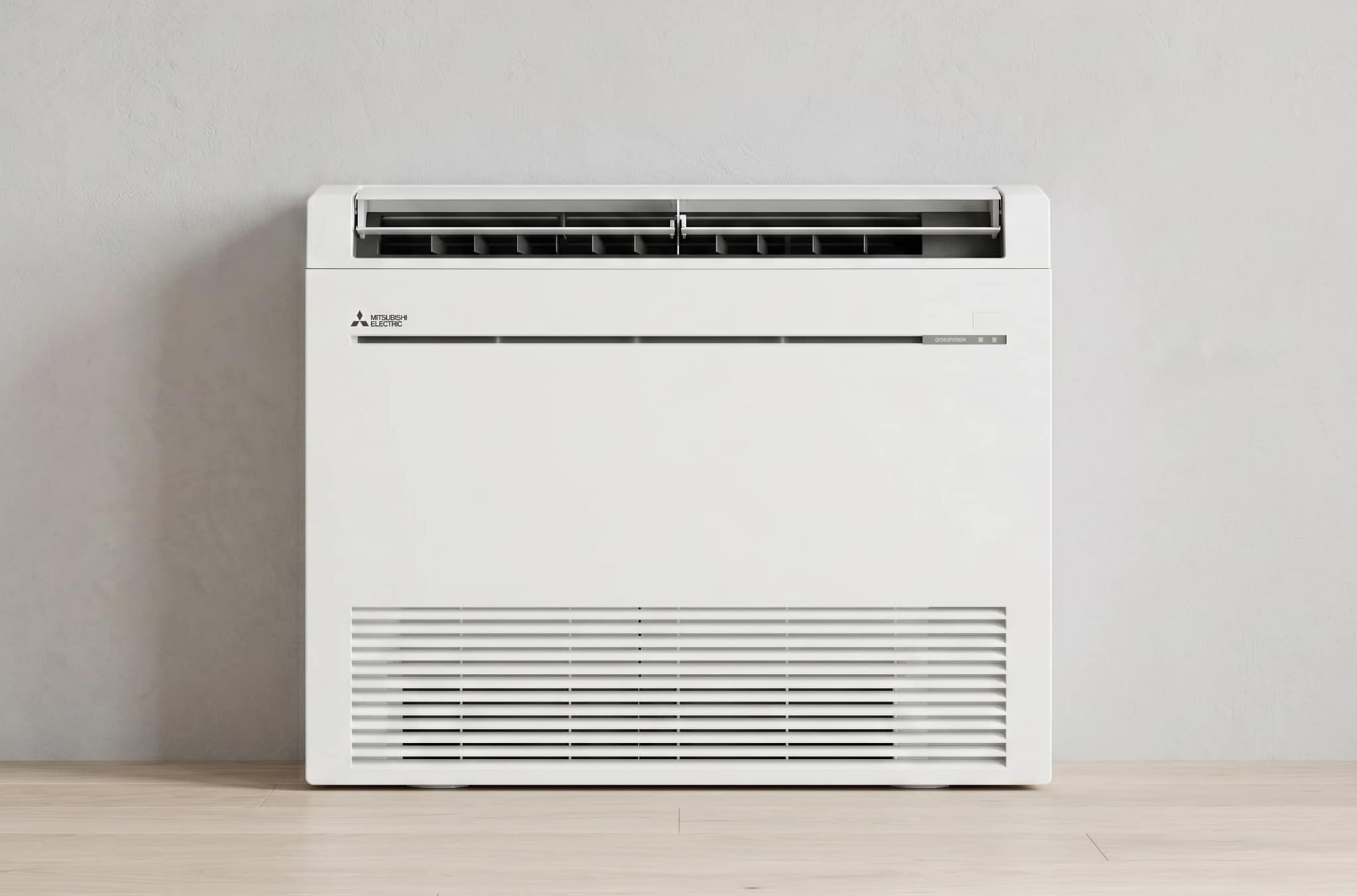 Mitsubishi Electric floor console heat pump showing upper discharge vent and lower return air grille, installed against a wall at floor level