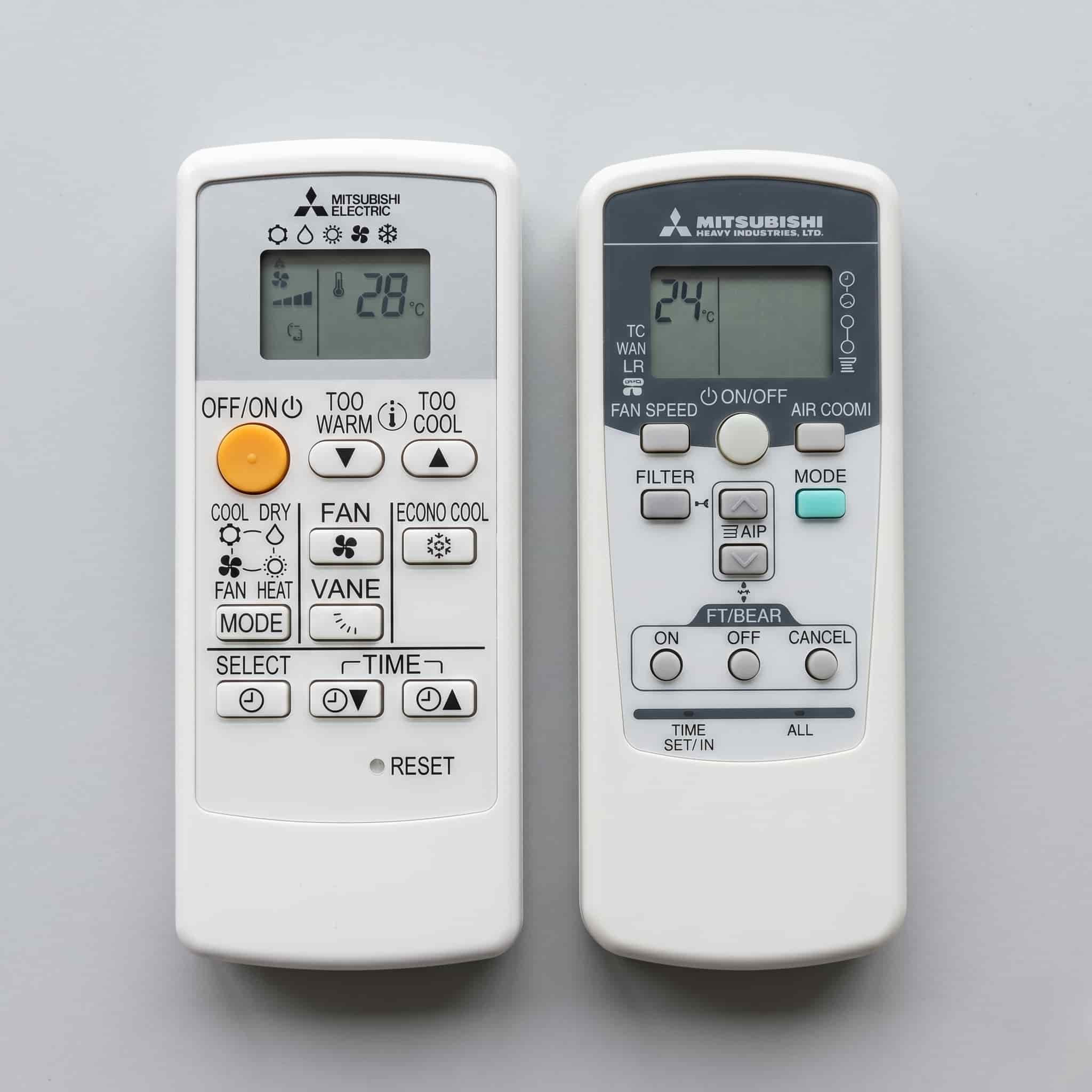 Mitsubishi Electric and Mitsubishi Heavy Industries heat pump remotes side by side showing different button layouts and branding