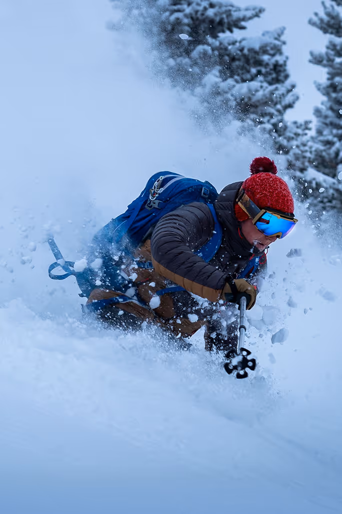 Skier with a red helmet skiing down a slope with powdery snow an pine trees in the background