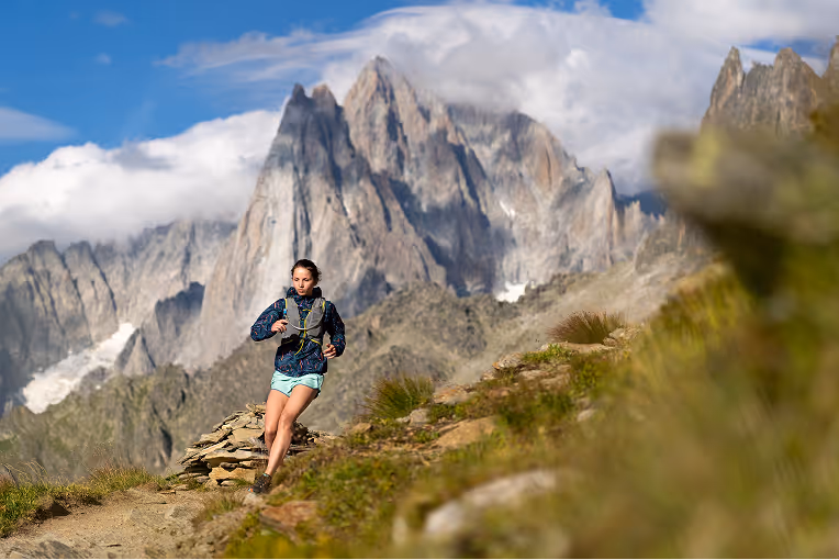 A mountain athlete performing a deep hip flexor stretch outdoors with a mountain landscape in the background