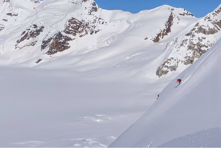 Skier riding down a snowy mountain with a scenic mountain view in the background