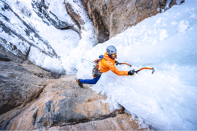 Ice climber climbing up an ice wall with ice picks