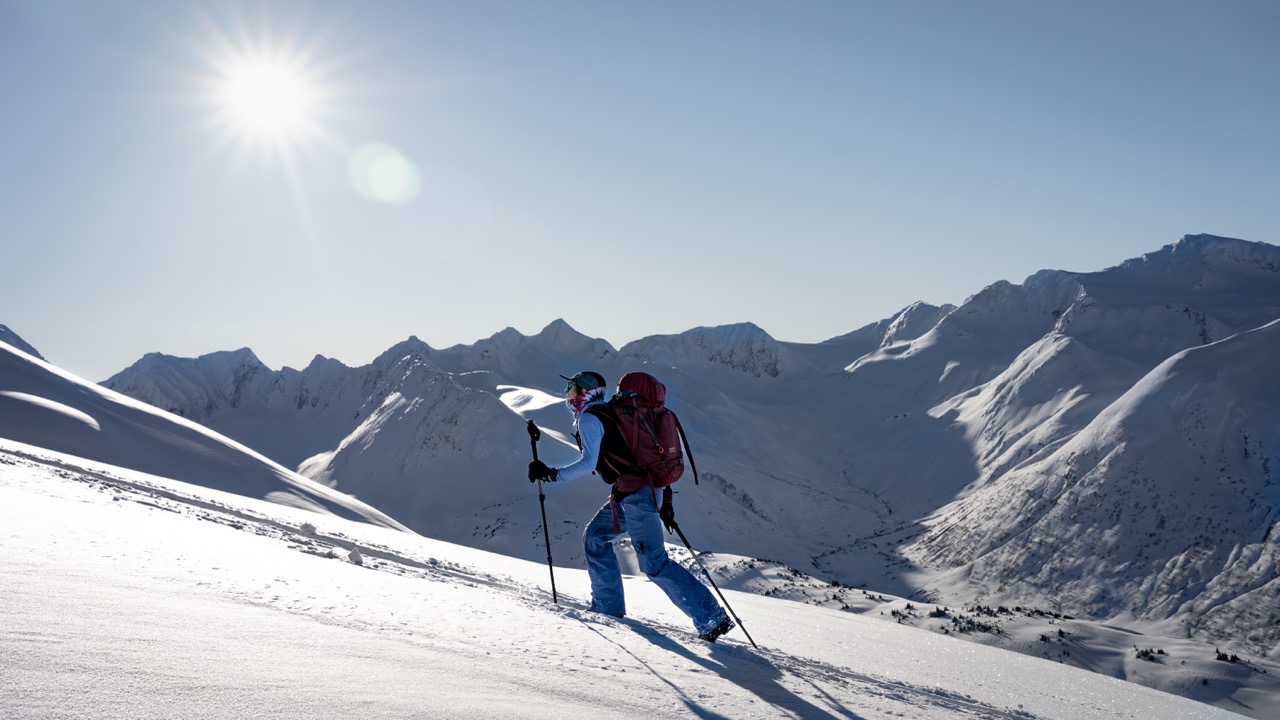 A split boarder on a split board tour ascending a snowy mountain with a mountainous view in the background.