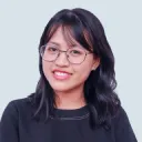 Smiling woman with shoulder-length black hair and glasses wearing a black top against a light background.