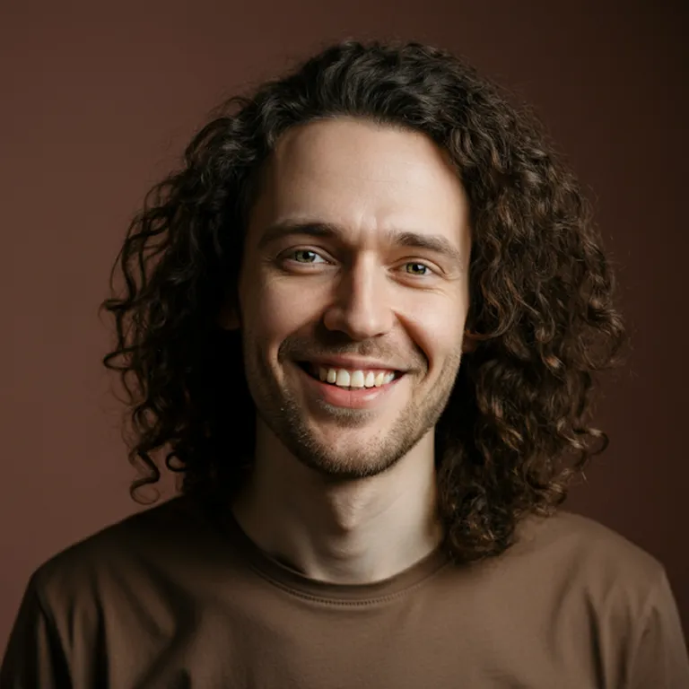 Smiling man with curly hair wearing a brown shirt against a brown background.