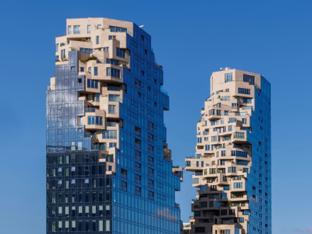 Moderne torens met unieke gevel met onregelmatige uitsteeksels en glanzende ramen onder een blauwe lucht.