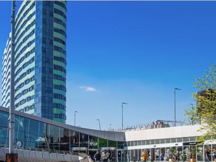 Moderne hoogbouw met een ronde glazen gevel naast een lager kantoorgebouw onder een heldere blauwe lucht.