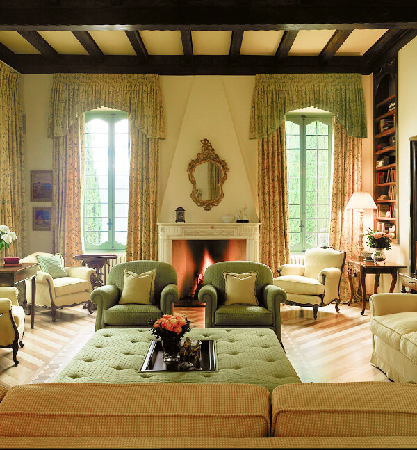 Outdoor seating area with two wicker chairs and a small table overlooking a lake surrounded by lush green mountains under a partly cloudy sky.