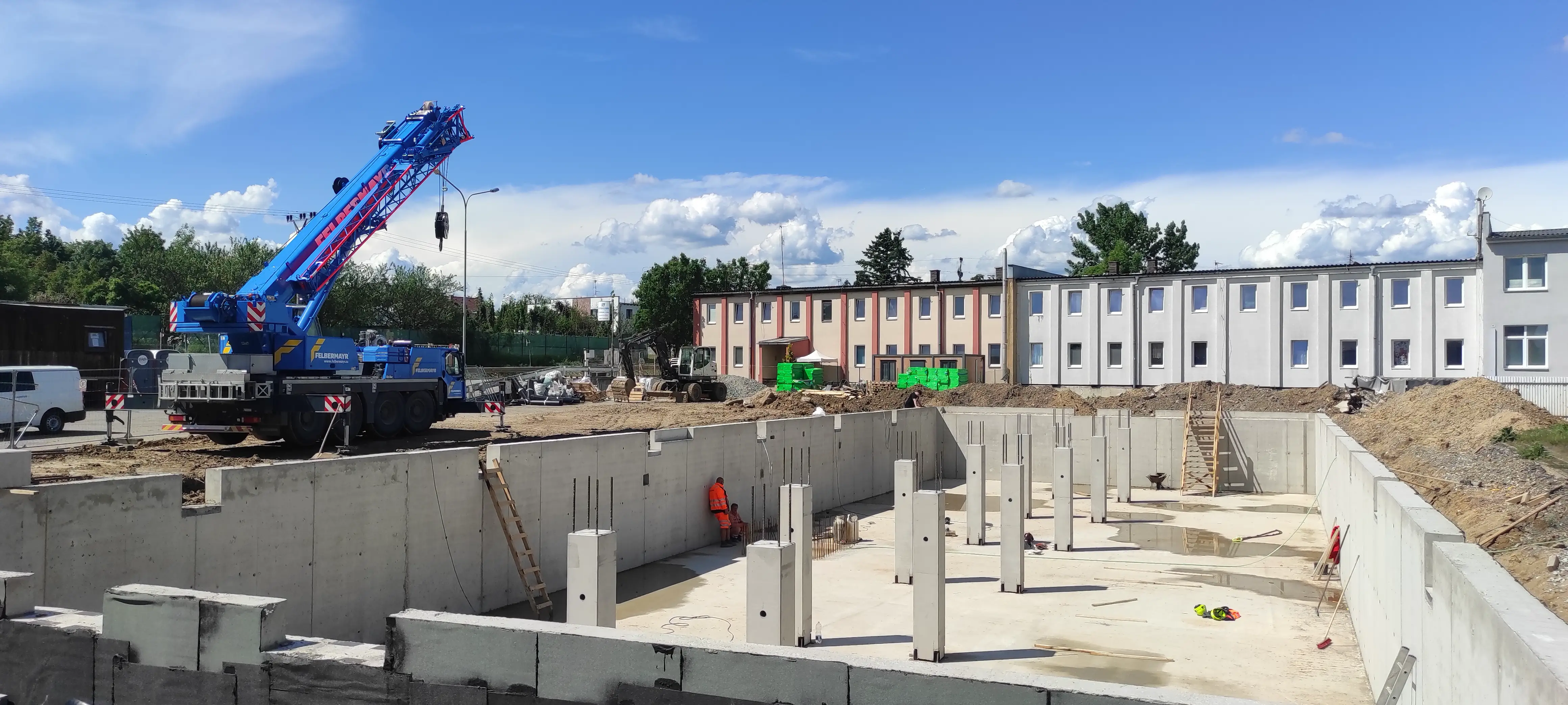 Hrubá stavba řadových domů s připravenou konstrukcí střechy a uskladněným stavebním materiálem