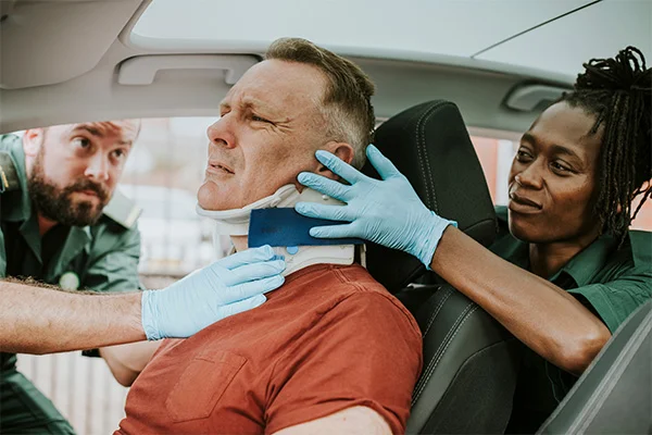 Emergency responders applying a neck brace to a man seated inside a car.