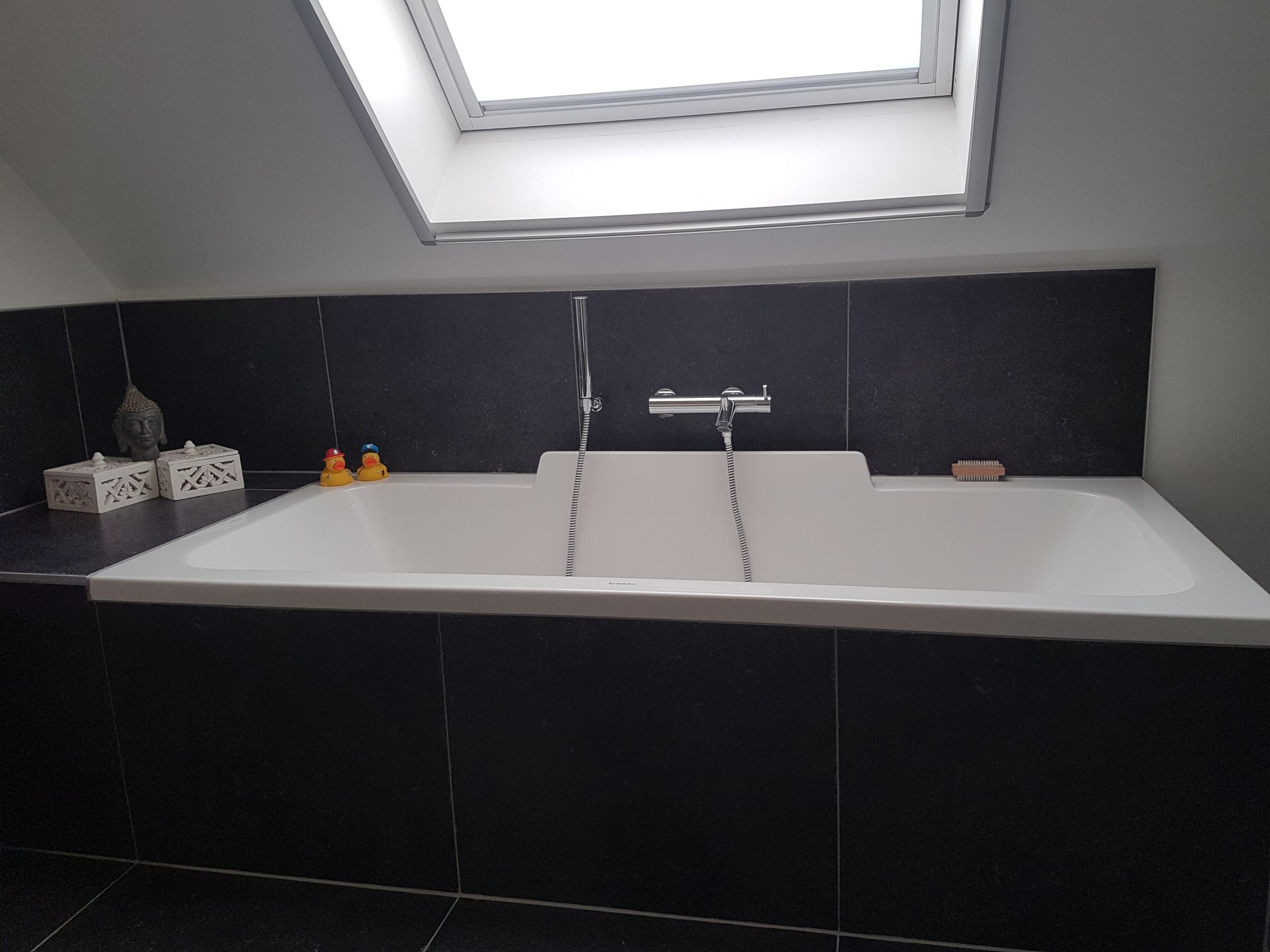 Badkamerrenovatie met ligbad onder dakraam en zwarte tegelwand door Sanyvan