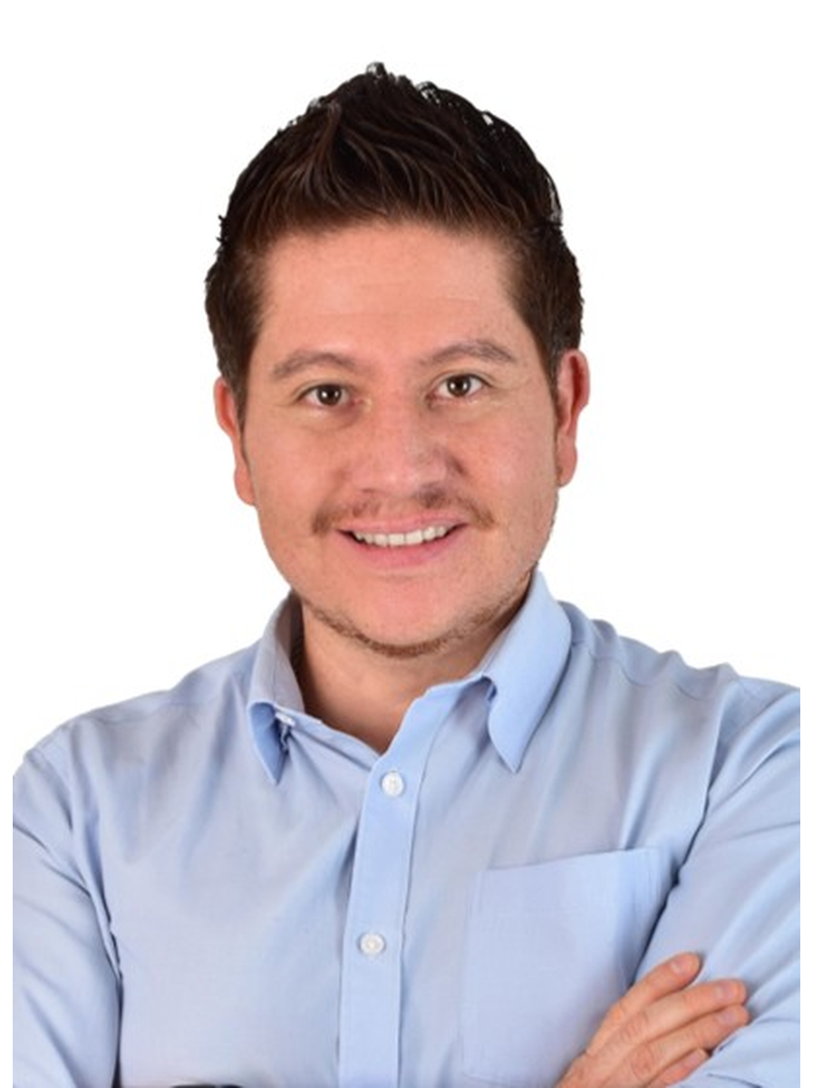 Smiling man with short dark hair wearing a light blue button-up shirt with arms crossed.