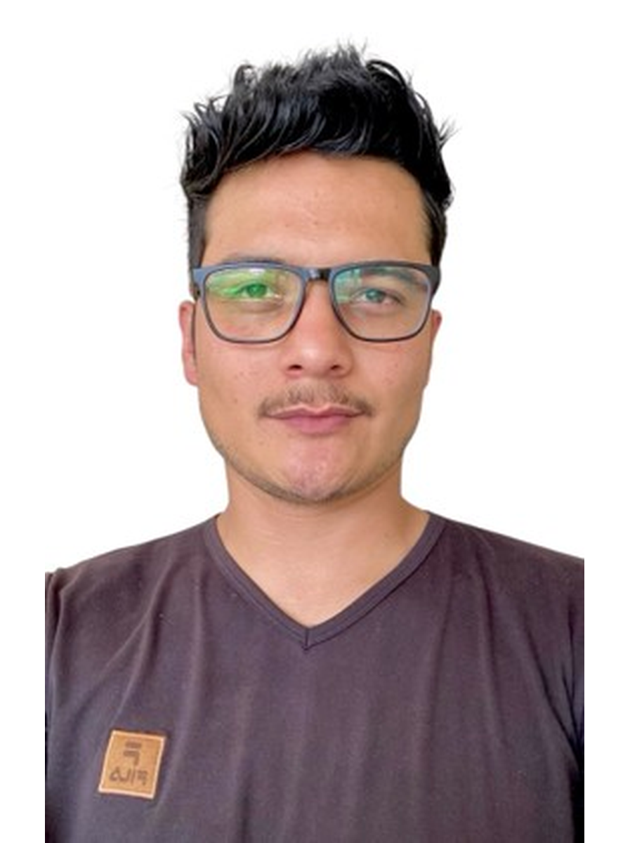 Portrait of a young man with short black hair, wearing glasses and a dark V-neck shirt with a small patch on the left side.