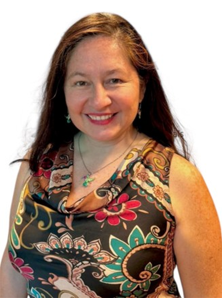 Smiling woman with long brown hair wearing a sleeveless floral patterned top and green cross necklace.