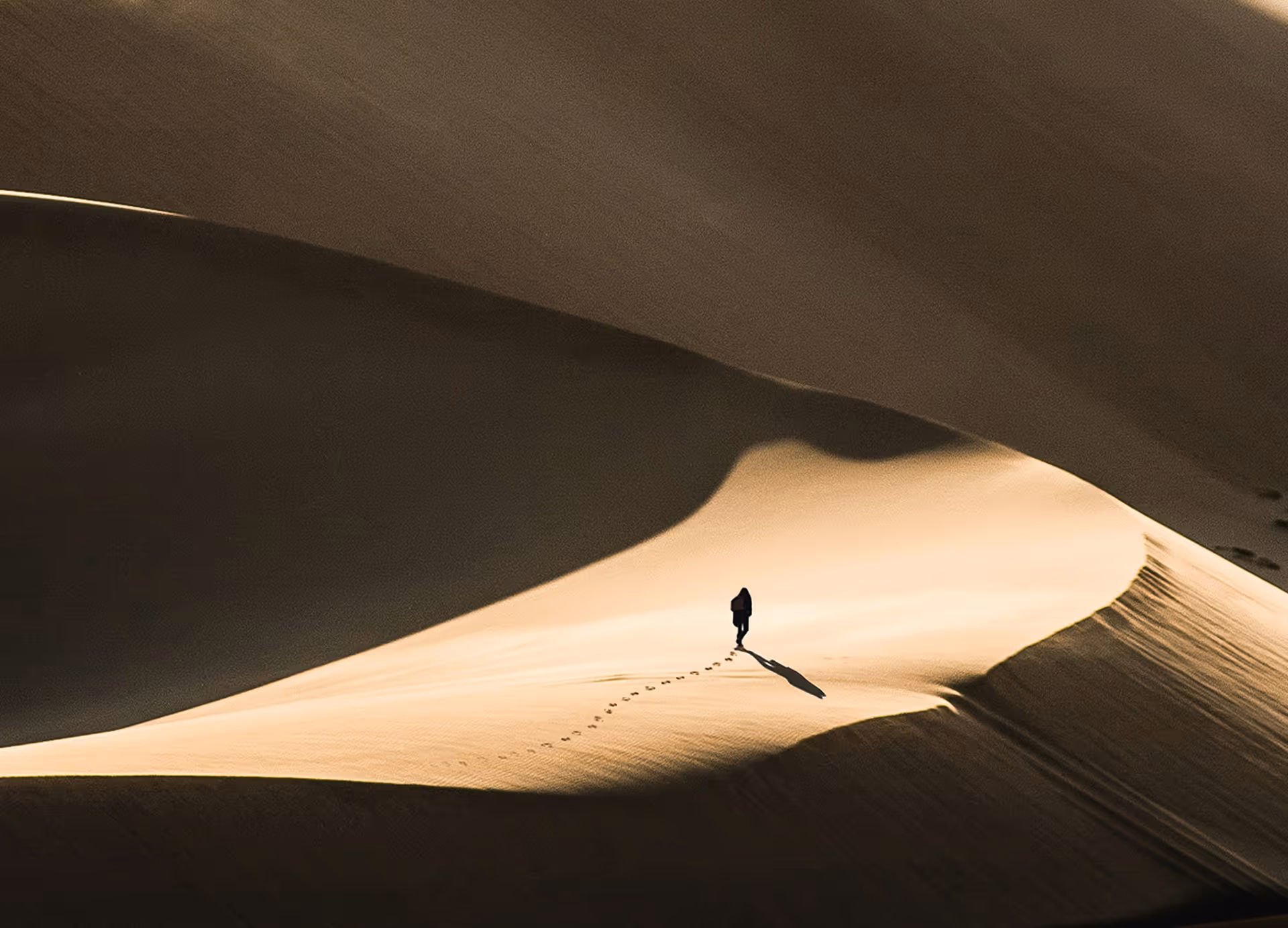 Person, der allein auf einer großen Sanddüne wandert und lange Schatten wirft.