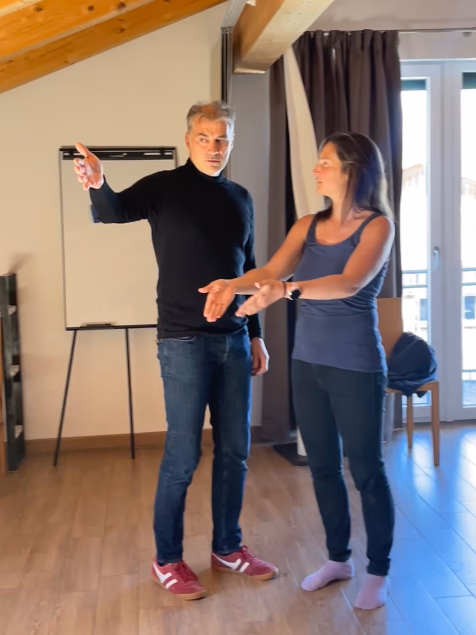 Ein Mann und eine Frau stehen in einem Raum und machen ausgedehnte Handgesten miteinander.