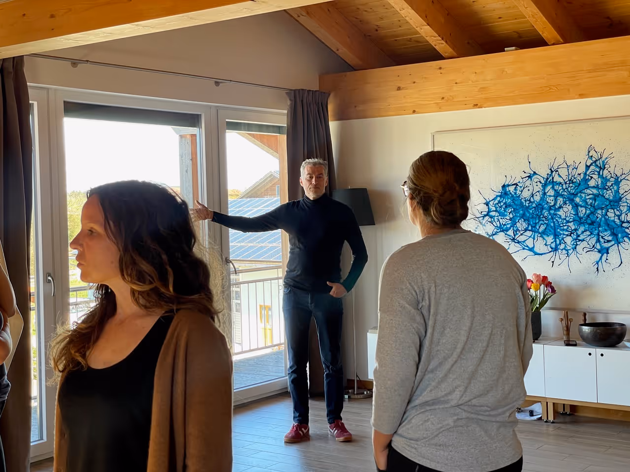 Drei Personen in einem modernen Raum mit Holzdecke, eine Person spricht und zeigt gestikulierend zur Seite.