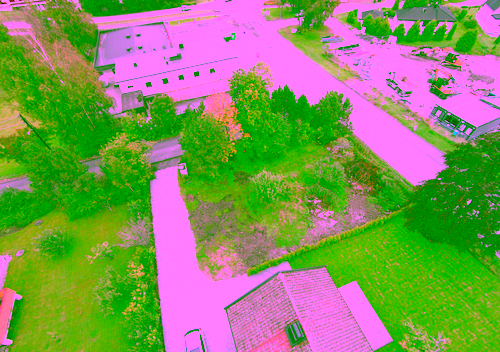 Luftfoto av en boligeiendom med en oppkjørsel, gressplen og trær, med en vei og flere bygninger i bakgrunnen.