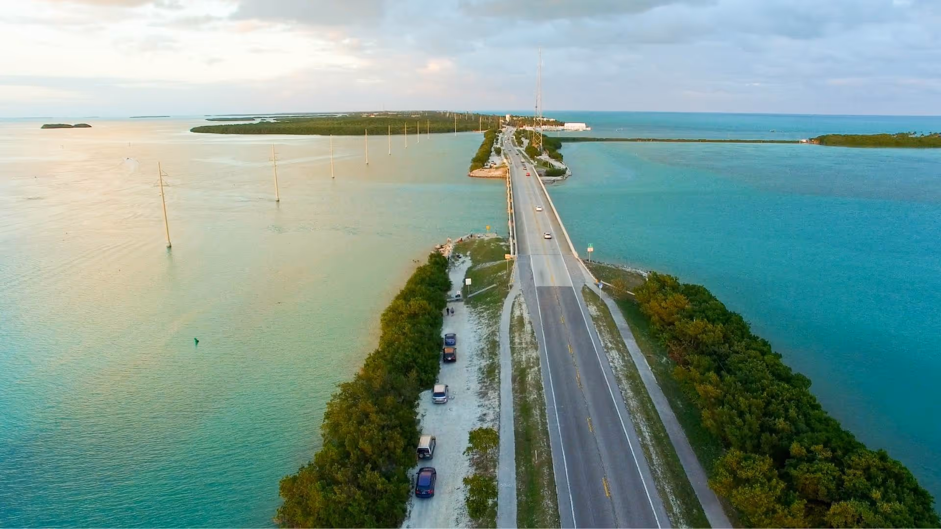 Aerial view of a Islamorada bridge crossing turquoise and green waters with cars driving and parked alongside green foliage.