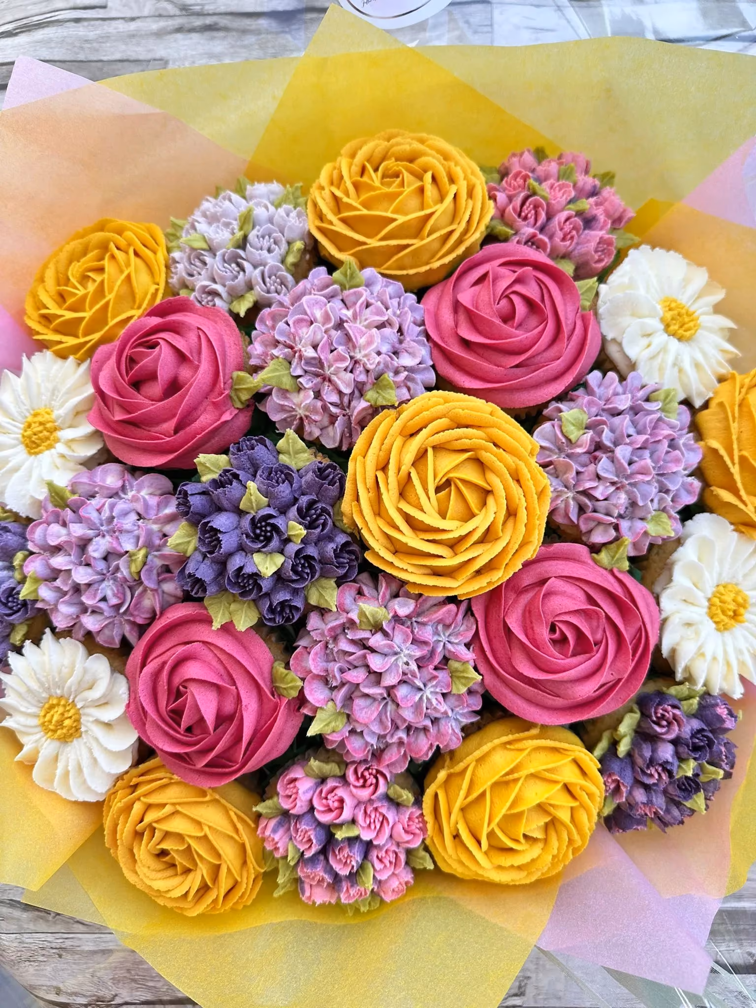 Bouquet of colorful buttercream flowers resembling roses, hydrangeas, and daisies on a wooden surface.