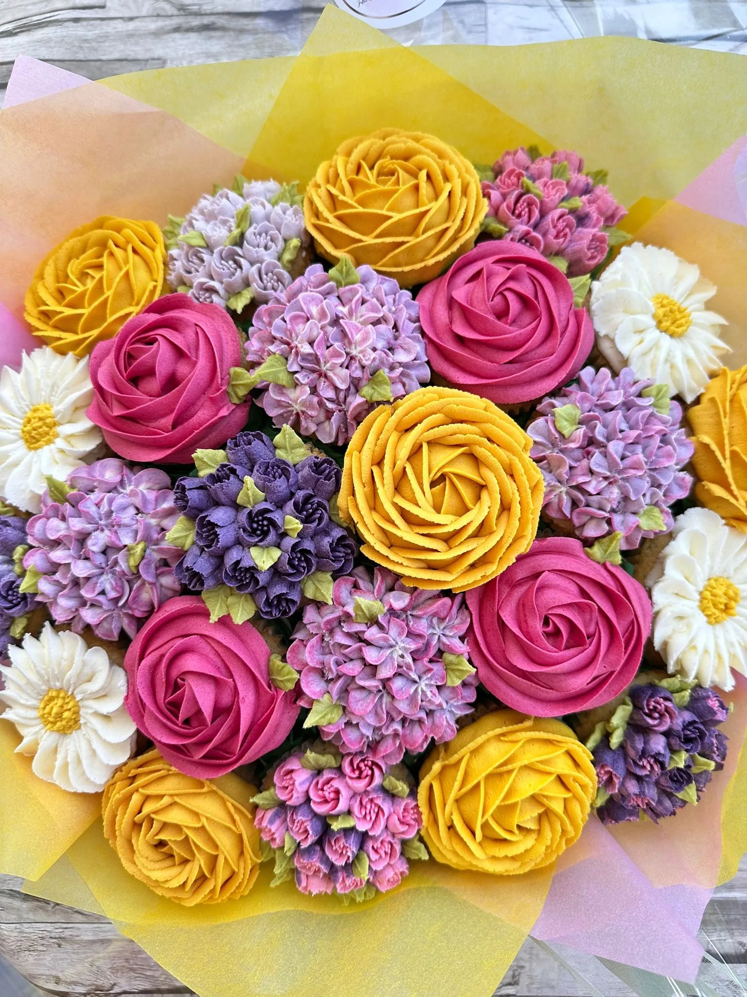 Bouquet of colorful buttercream flowers resembling roses, hydrangeas, and daisies on a wooden surface.