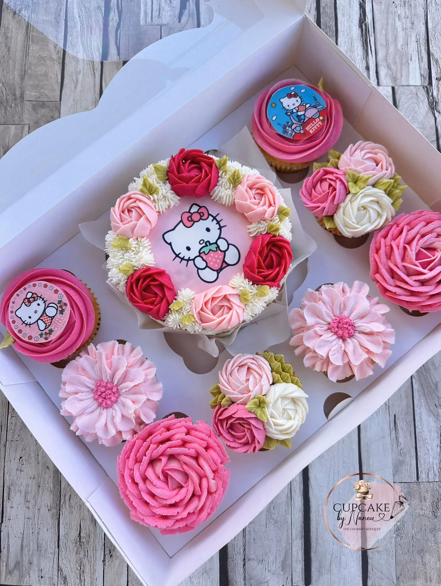 Box of Hello Kitty themed cupcakes and a cake decorated with pink, red, and white floral frosting.