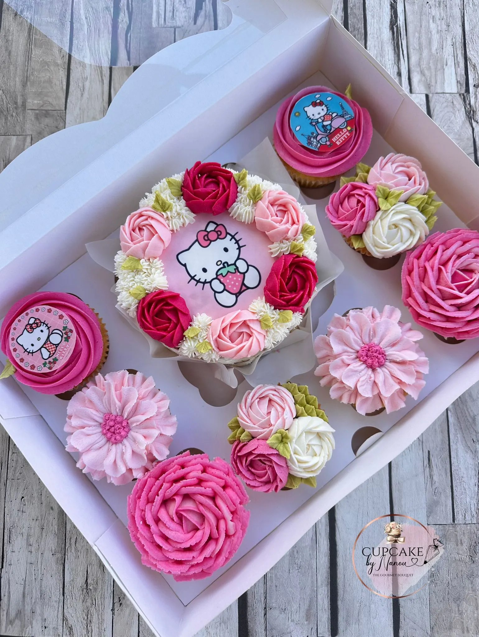 Box of Hello Kitty themed cupcakes and a cake decorated with pink, red, and white floral frosting.