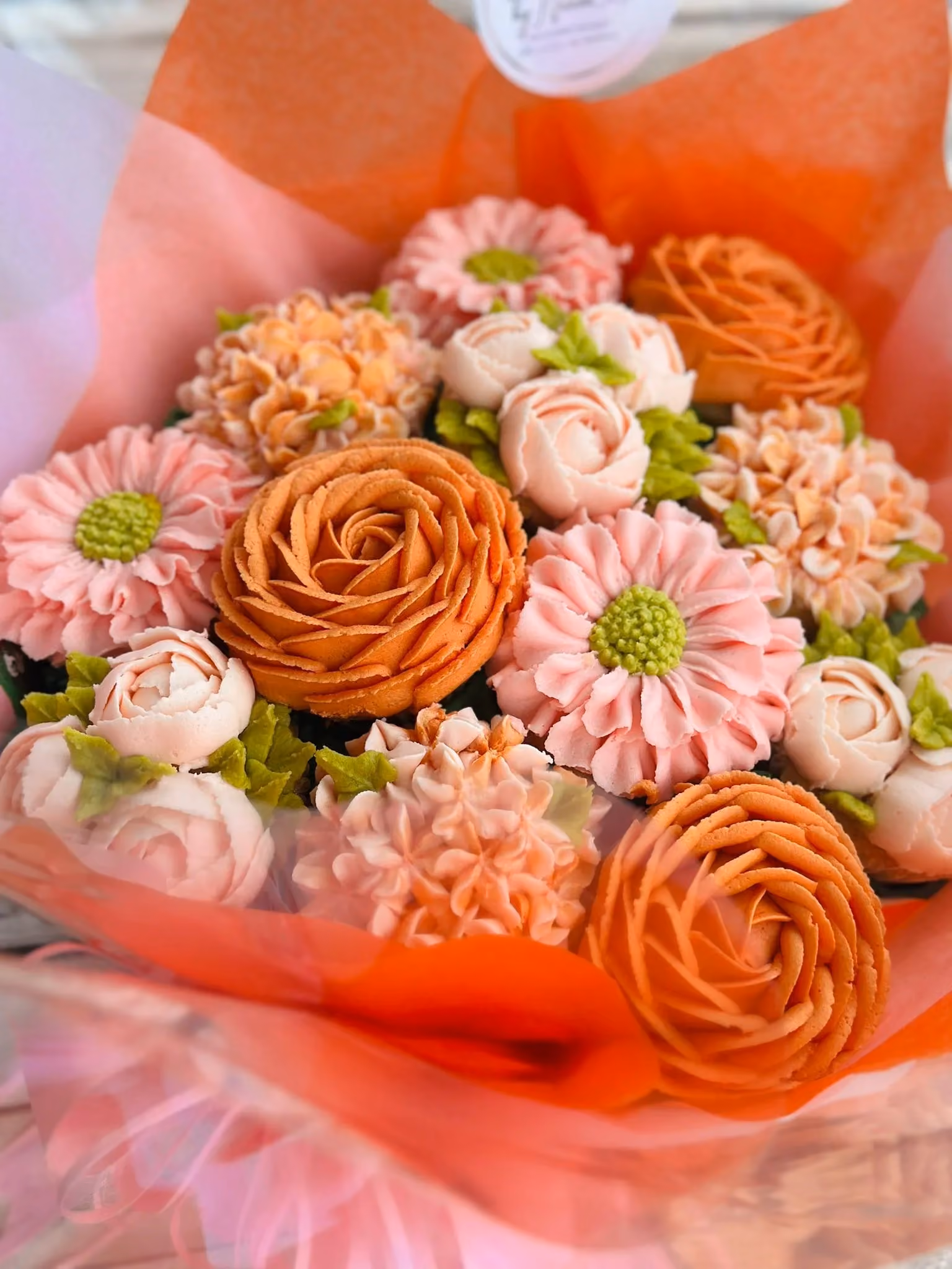 Close-up of a bouquet with orange and pink buttercream flowers wrapped in orange and pink tissue paper.