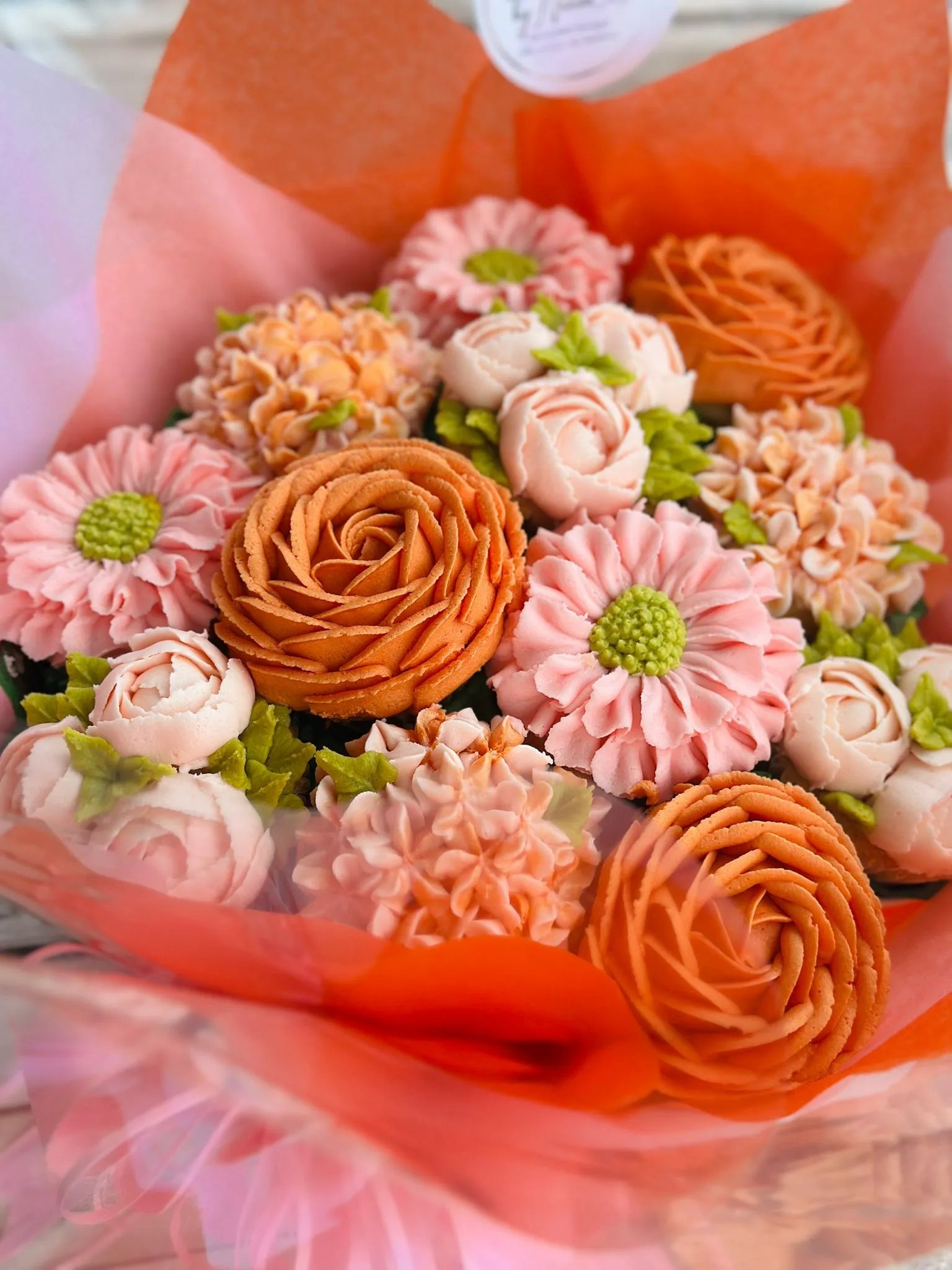 Close-up of a bouquet with orange and pink buttercream flowers wrapped in orange and pink tissue paper.